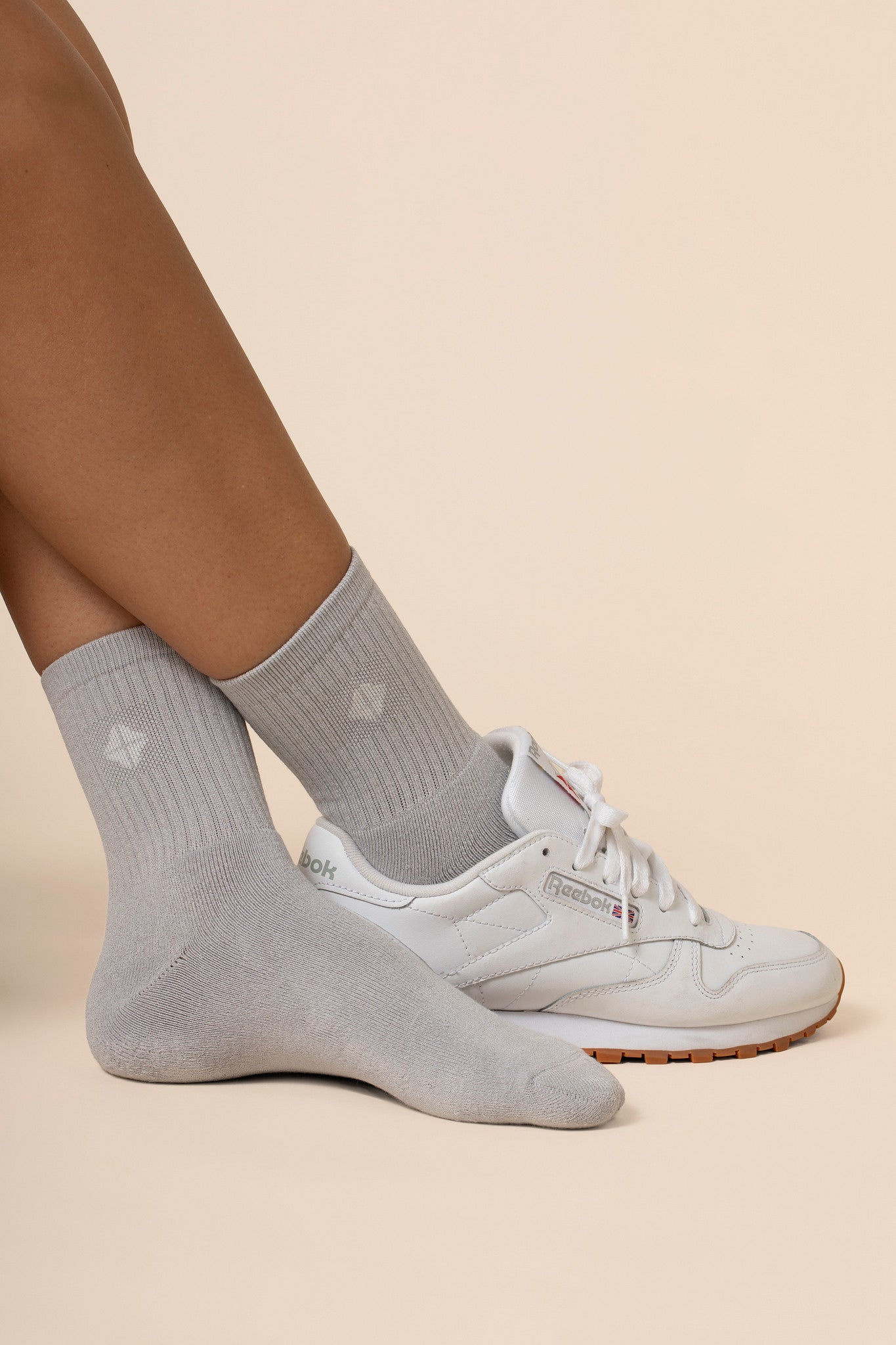 Gray crew socks worn with white sneakers on a beige background