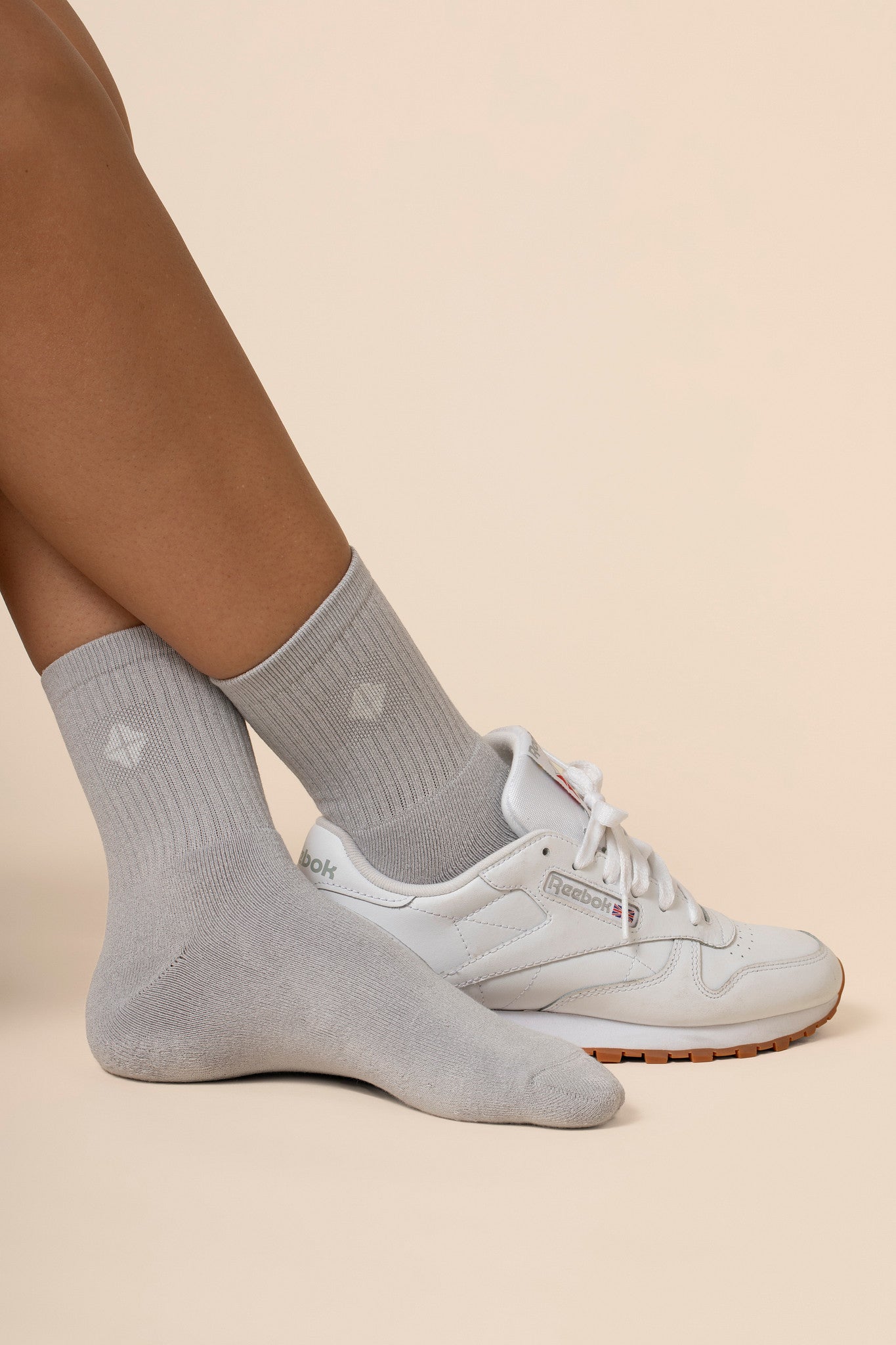 Gray crew socks worn with white sneakers on a beige background