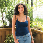 Woman wearing a blue tank top and jeans standing outdoors with plants in the background