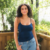 Woman wearing a blue tank top and jeans standing outdoors with plants in the background