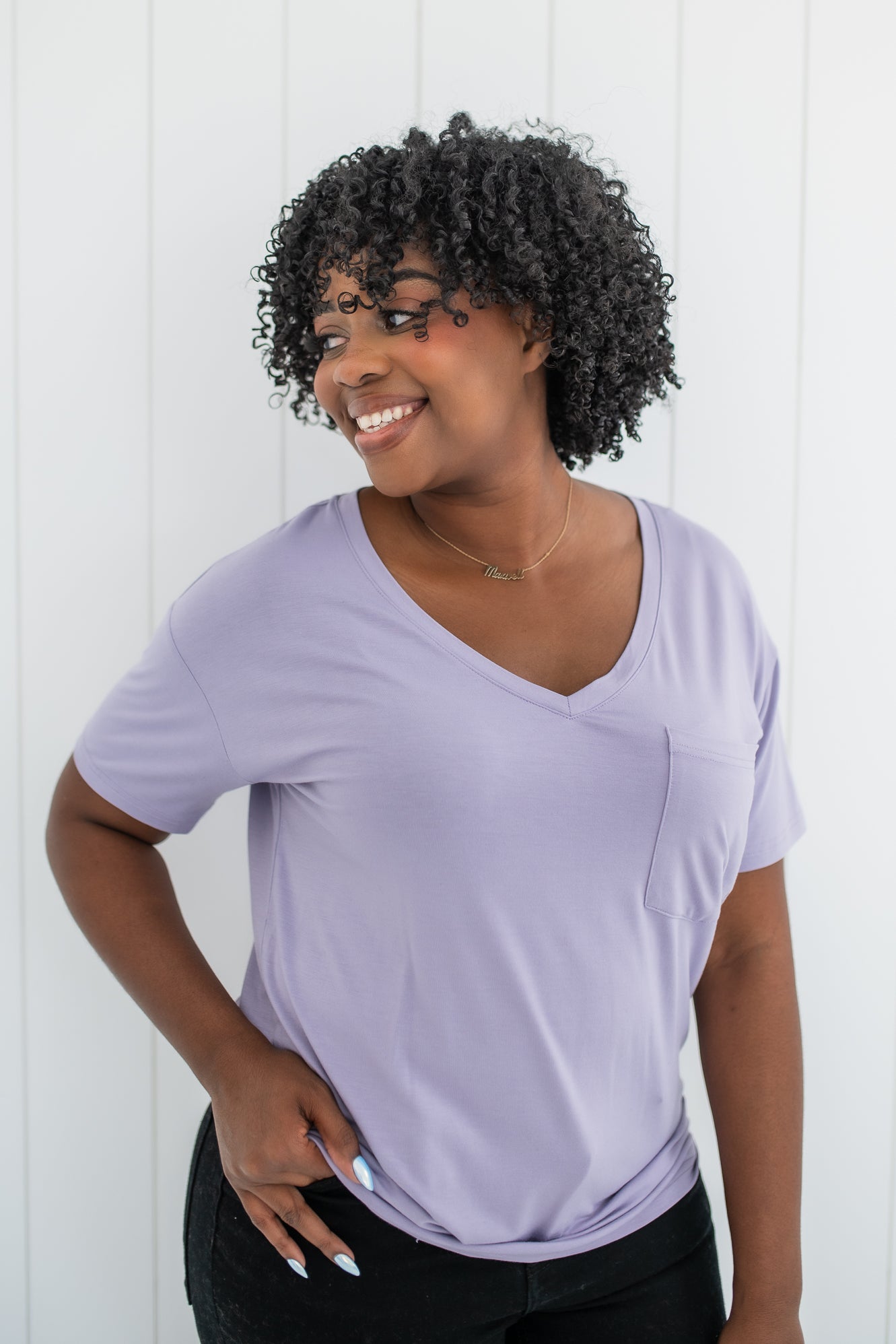 Model looking to the side with hand on hip and wearing the Kyte Women's V Neck in Taro paired with dark jeans