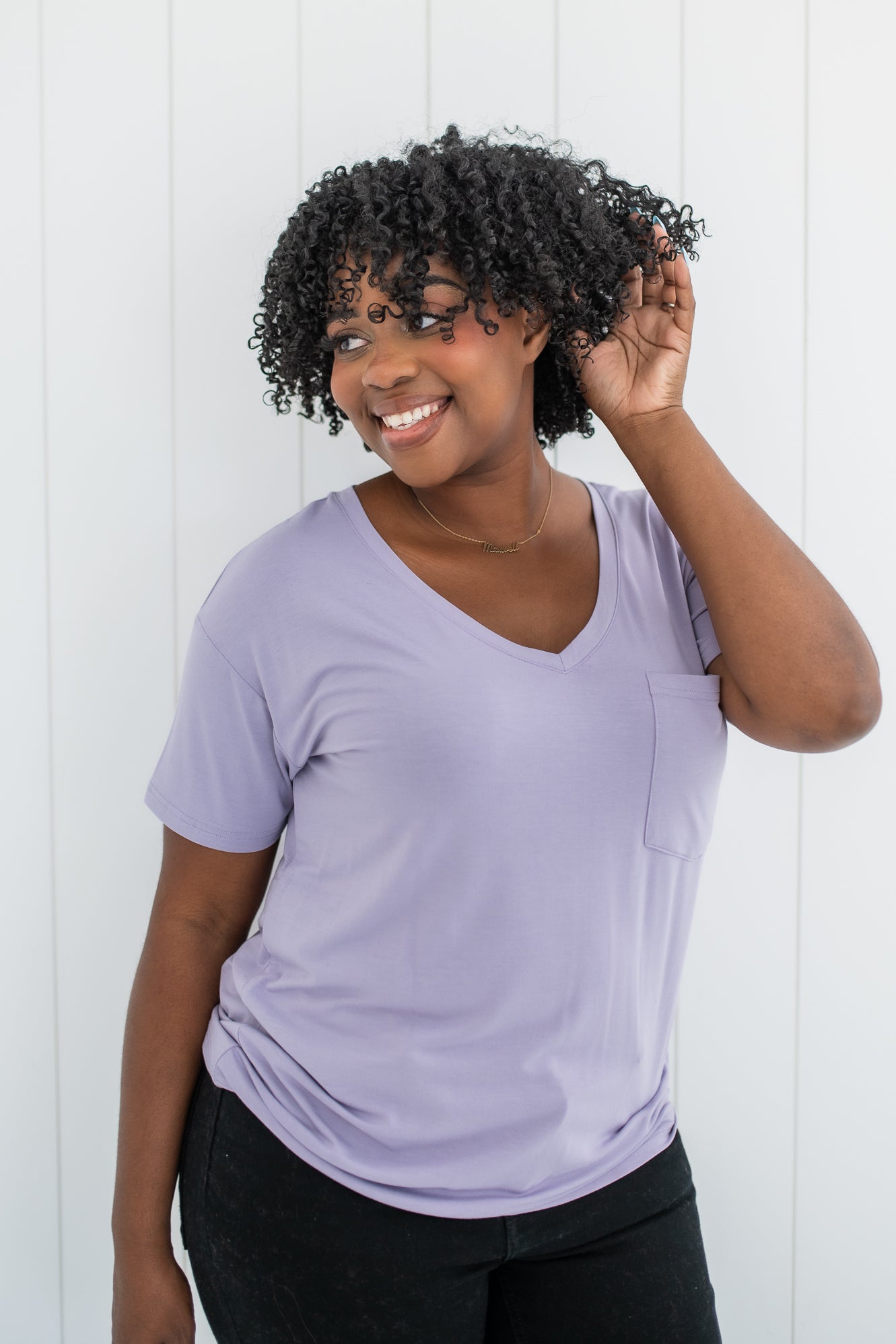 Woman with hand in hair while modeling the Women's V Neck in Taro paired with dark jeans