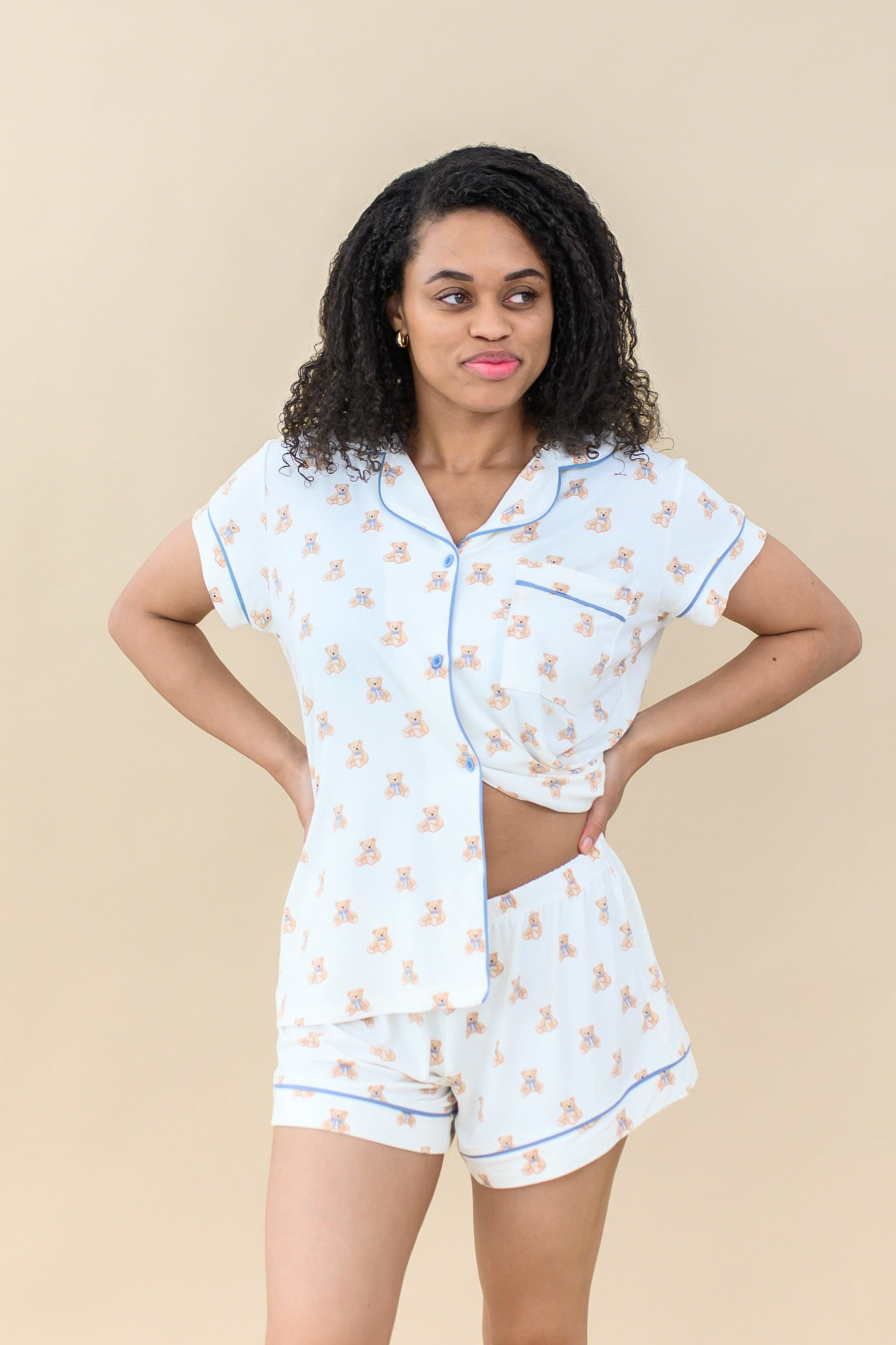 Model wearing Women’s Short Sleeve Pajama Set in Teddy Bear holding pajama top slightly up to show waistband of pajama short