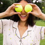 Woman holding two tennis balls over their eyes while modeling the Women's Short Sleeve Pajama Set in Tennis