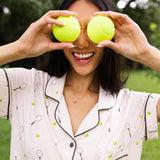 Woman holding two tennis balls over their eyes while modeling the Women's Short Sleeve Pajama Set in Tennis