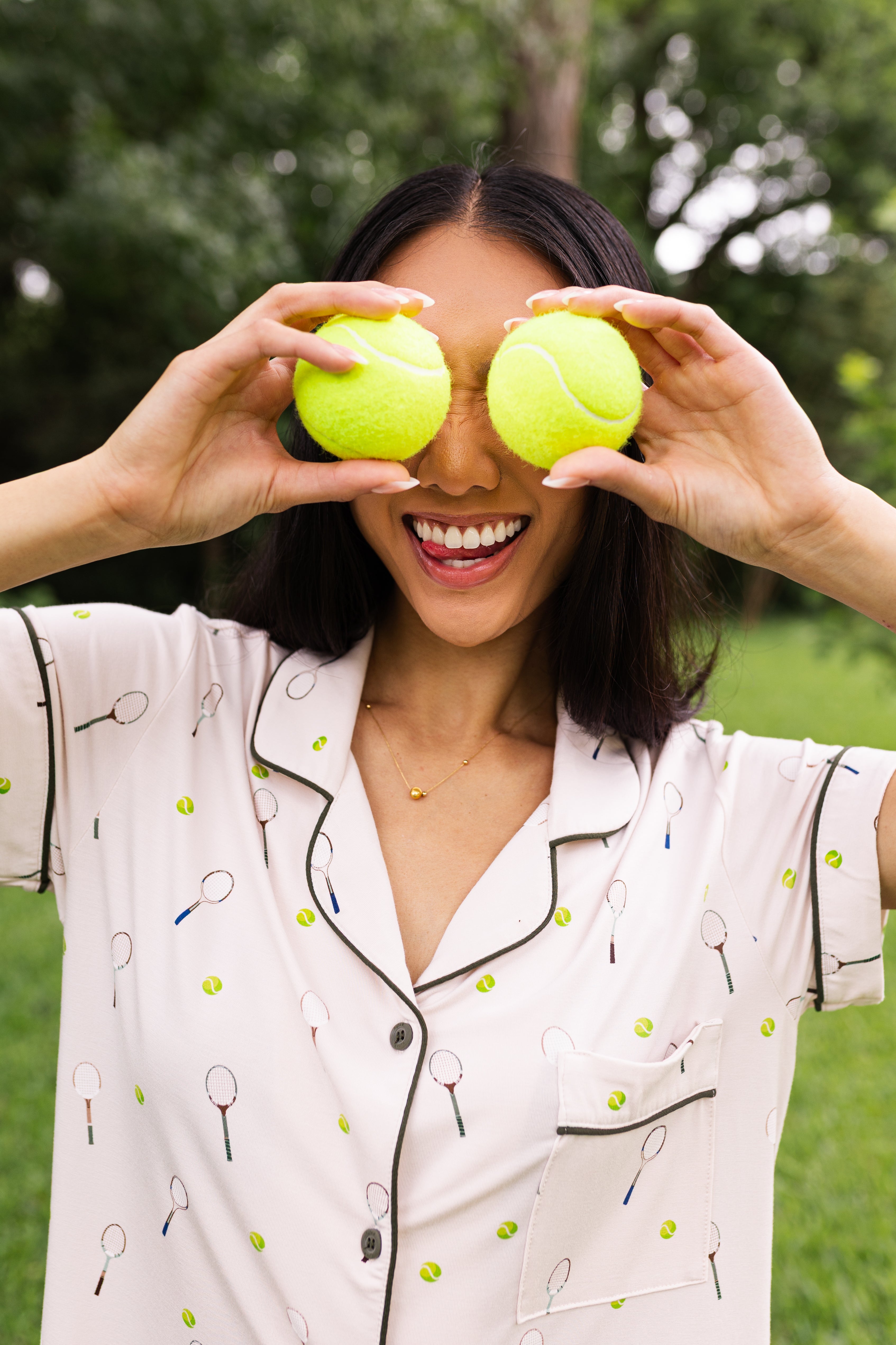 Woman holding two tennis balls over their eyes while modeling the Women's Short Sleeve Pajama Set in Tennis