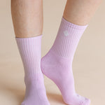 A close-up of a person's feet and lower legs wearing light lavender ribbed crew socks against a solid beige background.