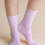 A close-up of a person's feet and lower legs wearing light lavender ribbed crew socks against a solid beige background.