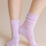 A close-up of a person's feet wearing light pink ribbed crew socks against a solid beige background.