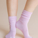 A close-up of a person's feet wearing light pink ribbed crew socks against a solid beige background.