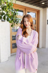 Woman wearing a light purple cardigan standing in front of a wooden door. ::: Model is 5'7" wearing size M ///