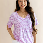 Model wearing Women's Relaxed Fit V-Neck in Thistle Leopard print over a white pant on a beige background