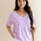 Model wearing Women's Relaxed Fit V-Neck in Thistle Leopard print over a white pant on a beige background
