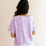 Back side of Women's Relaxed Fit V-Neck in Thistle Leopard print over a white pant on a beige background