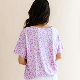 Back side of Women's Relaxed Fit V-Neck in Thistle Leopard print over a white pant on a beige background