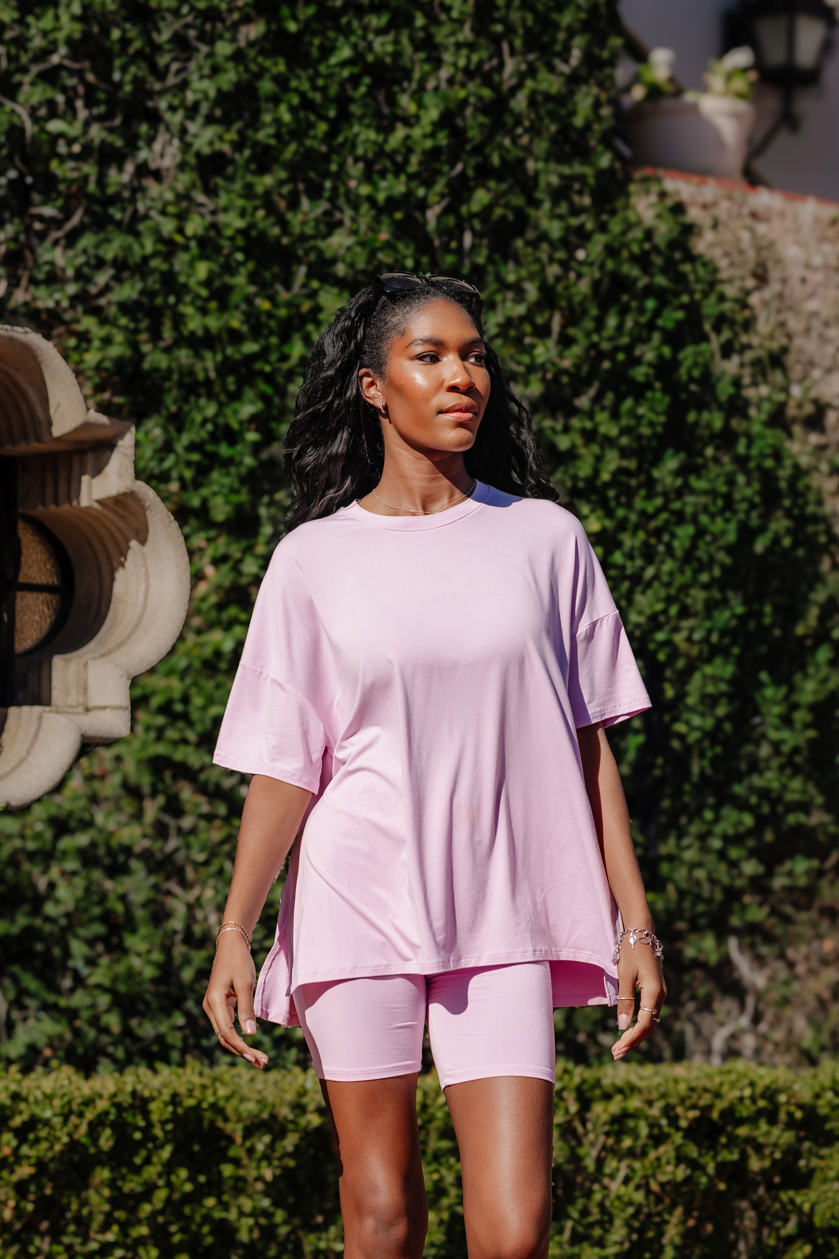 Model looking to the side while standing in front of a wall of greenery while wearing the Kyte Bamboo Women’s Biker Short Set in Thistle
