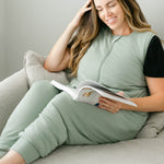 Female sitting on a couch reading a book wearing the Adult Sleep Bag Walker in Thyme