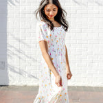 Female walking in front of a white brick wall wearing the Women’s Smocked Dress in Tulip
