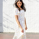 Female walking in front of a white brick wall wearing the Women’s Smocked Dress in Tulip