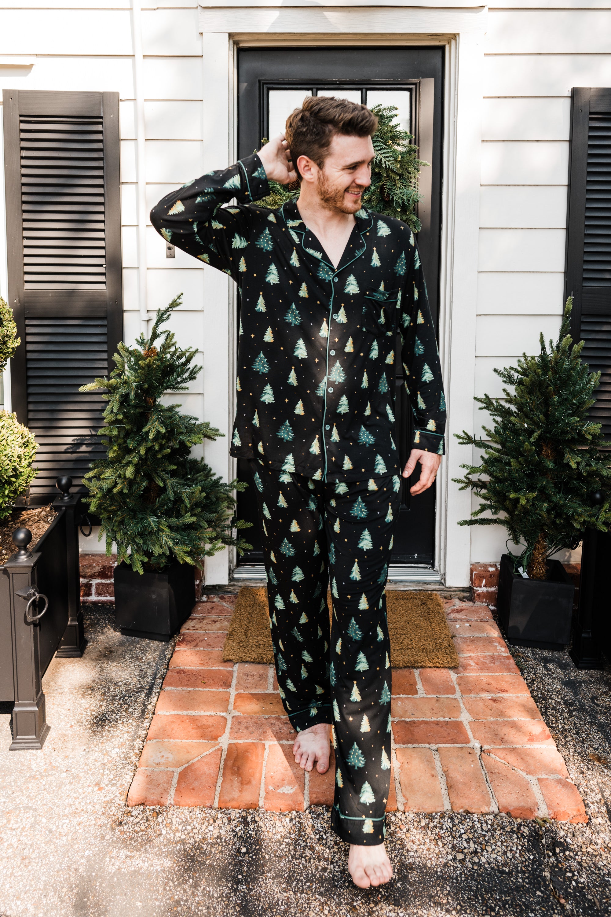 Model standing in front of a black door wearing the Men's Long Sleeve Pajama Set in Twinkle Tree