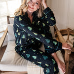 Model sitting partially curled up in a chair while wearing the Women's Long Sleeve Pajama Set in Twinkle Tree