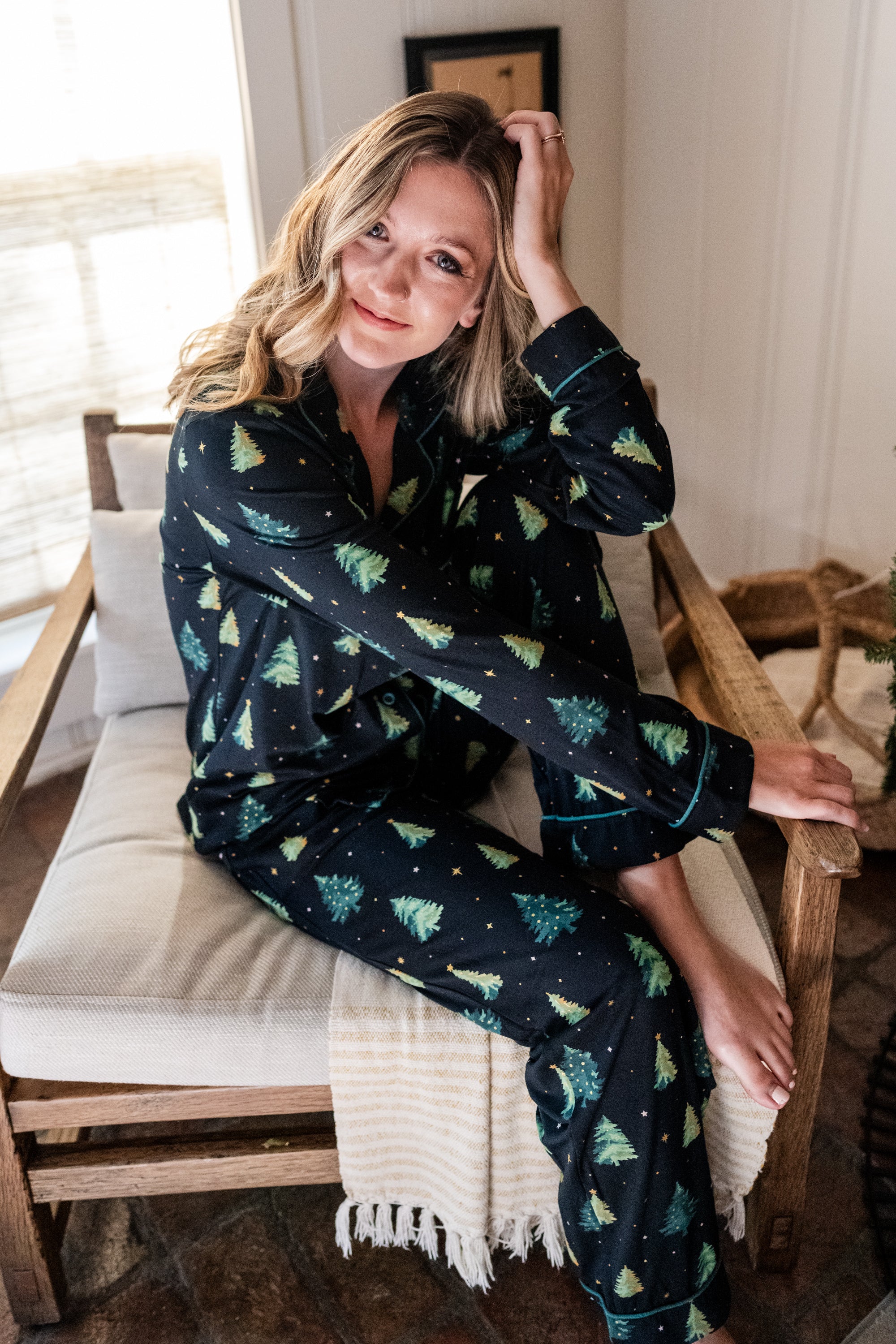 Model sitting partially curled up in a chair while wearing the Women's Long Sleeve Pajama Set in Twinkle Tree