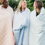 3 women modeling Bamboo Quilt Blankets in a wildflower field in the colors Canyon, Mist and Dew