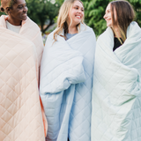 3 women modeling Bamboo Quilt Blankets in a wildflower field in the colors Canyon, Mist and Dew