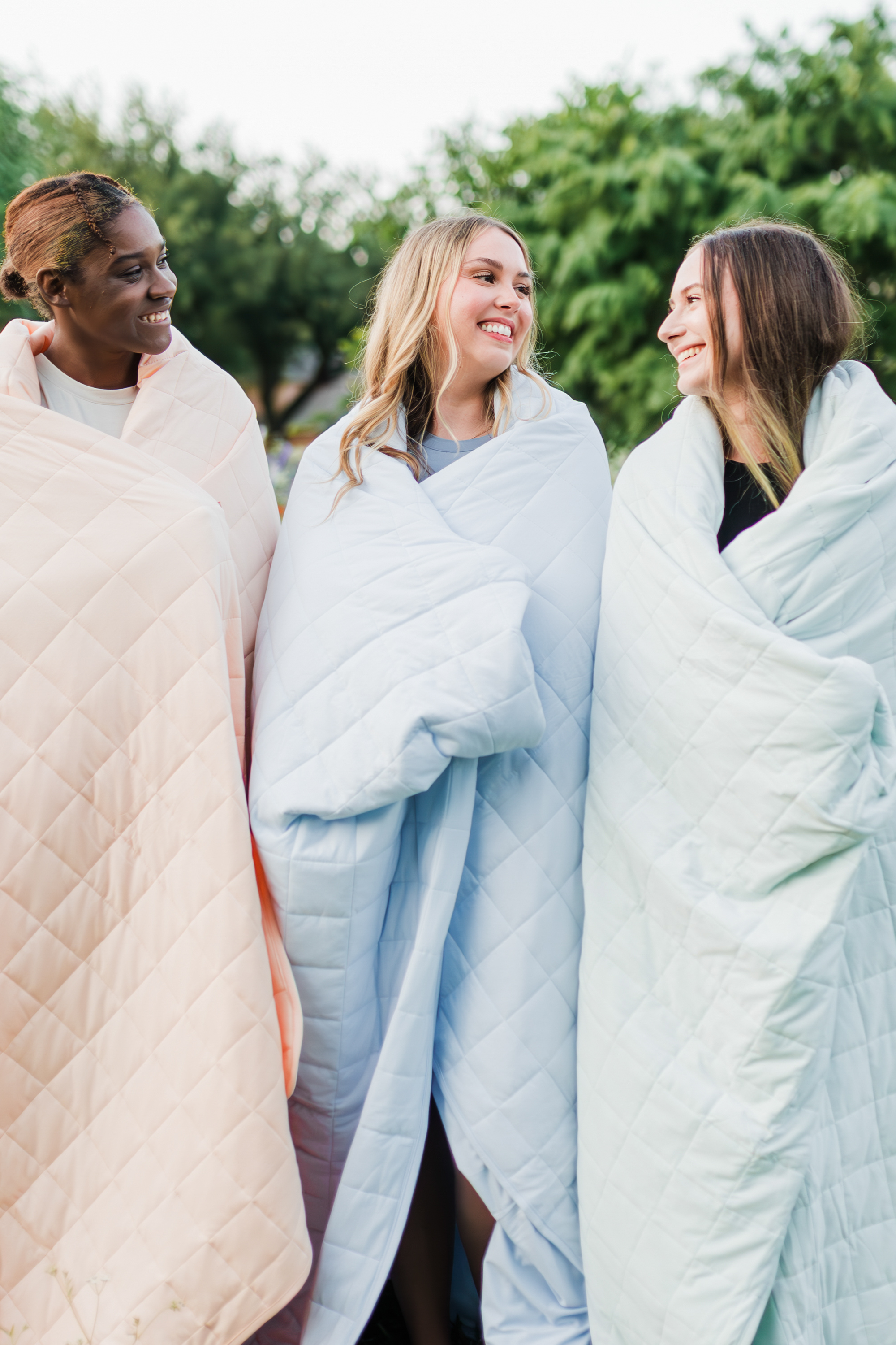 3 women modeling Bamboo Quilt Blankets in a wildflower field in the colors Canyon, Mist and Dew