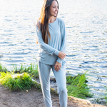 Woman modeling light blue jogger set in an outdoor setting with lake in backdrop