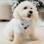 Small white dog standing on a cream carpet in front of a lit and frosted tree wearing the Dog Bandana in Vintage Santa
