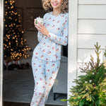Female model leaning against a door frame on a White House wearing the Women's Jogger Pajama Set in Vintage Santa holding a mug of coffee in her hands