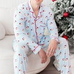 Man wearing light blue pajamas with santa pattern sitting on a white couch next to christmas tree