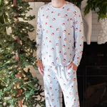 Smiling male model standing in front of a white brick fireplace with white stockings hung on the mantel wearing the Men's Jogger Set in Vintage Santa with one hand in the pants pocket