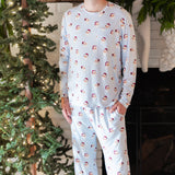 Smiling male model standing in front of a white brick fireplace with white stockings hung on the mantel wearing the Men's Jogger Set in Vintage Santa with one hand in the pants pocket