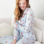 Woman wearing a light blue pajama set with red trim sitting on a white couch.