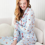 Woman wearing a light blue pajama set with red trim sitting on a white couch.