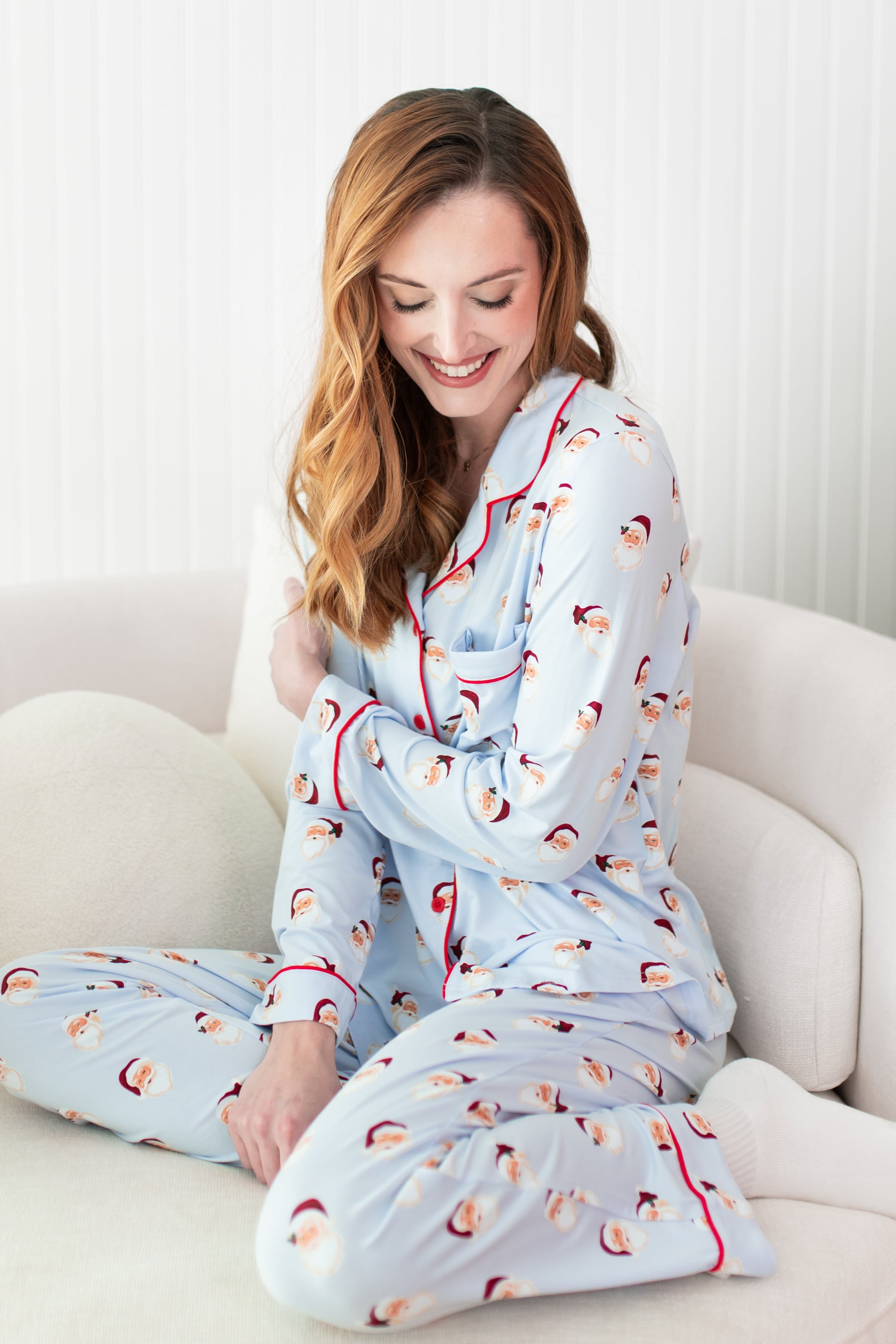 Woman wearing a light blue pajama set with red trim sitting on a white couch.
