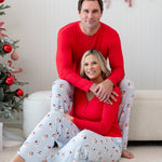 Husband wearing the Men's Lounge Pants in Vintage Santa and Cardinal Henley sitting on an ottoman with his wife in front of him matching in Vintage Santa Lounge pants and a Women's Cardinal Henley