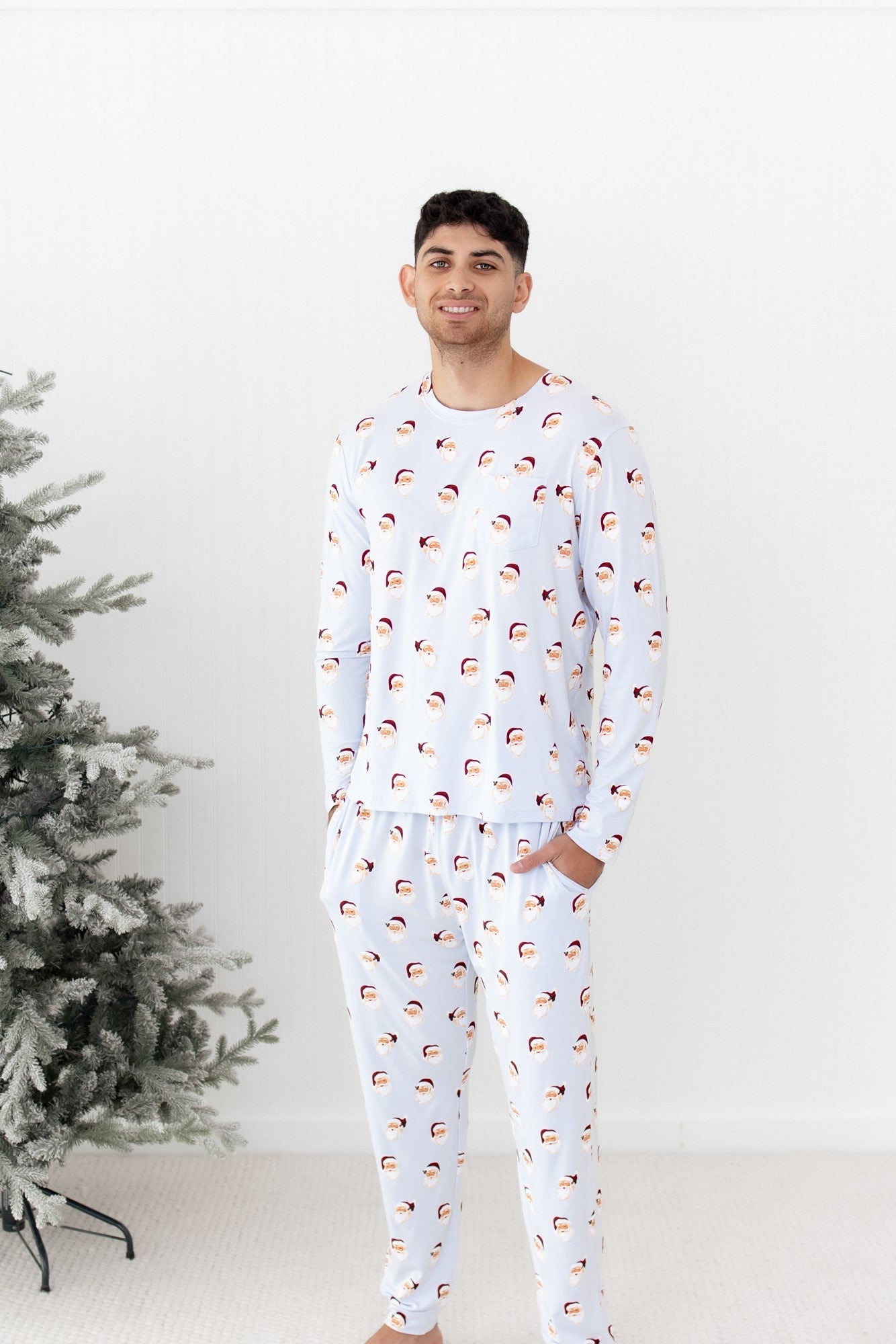 Male model standing beside a frosted tree wearing the Men's Jogger Set in Vintage Santa with his hands in the pants pockets