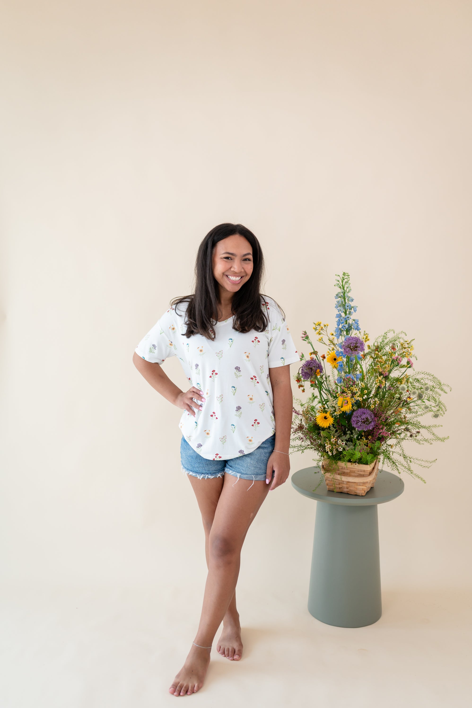 Woman modeling Women’s Relaxed Fit V-Neck in Wildflower and denim shorts next to a floral arrangement  