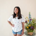 Woman modeling Women’s Relaxed Fit V-Neck in Wildflower next to a floral arrangement 