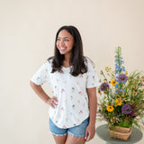 Woman modeling Women’s Relaxed Fit V-Neck in Wildflower next to a floral arrangement 
