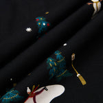 Close-up of a black fabric with a festive holiday print featuring snowmen, snowboards, decorated Christmas trees, and snowflakes.