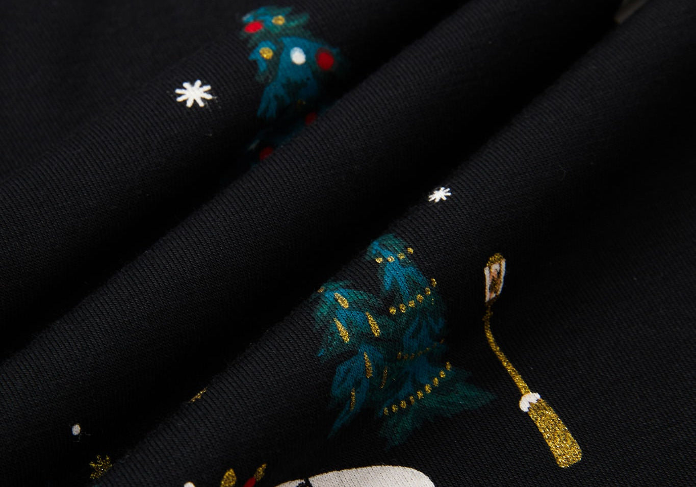 Close-up of a black fabric with a festive holiday print featuring snowmen, snowboards, decorated Christmas trees, and snowflakes.