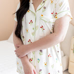 Woman wearing a white pajama set with floral patterns in a bedroom setting.