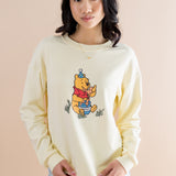 Person wearing a light-colored crewneck sweatshirt with a winnie the pooh graphic on a beige background ::: Model is 5'6" wearing size XS ///