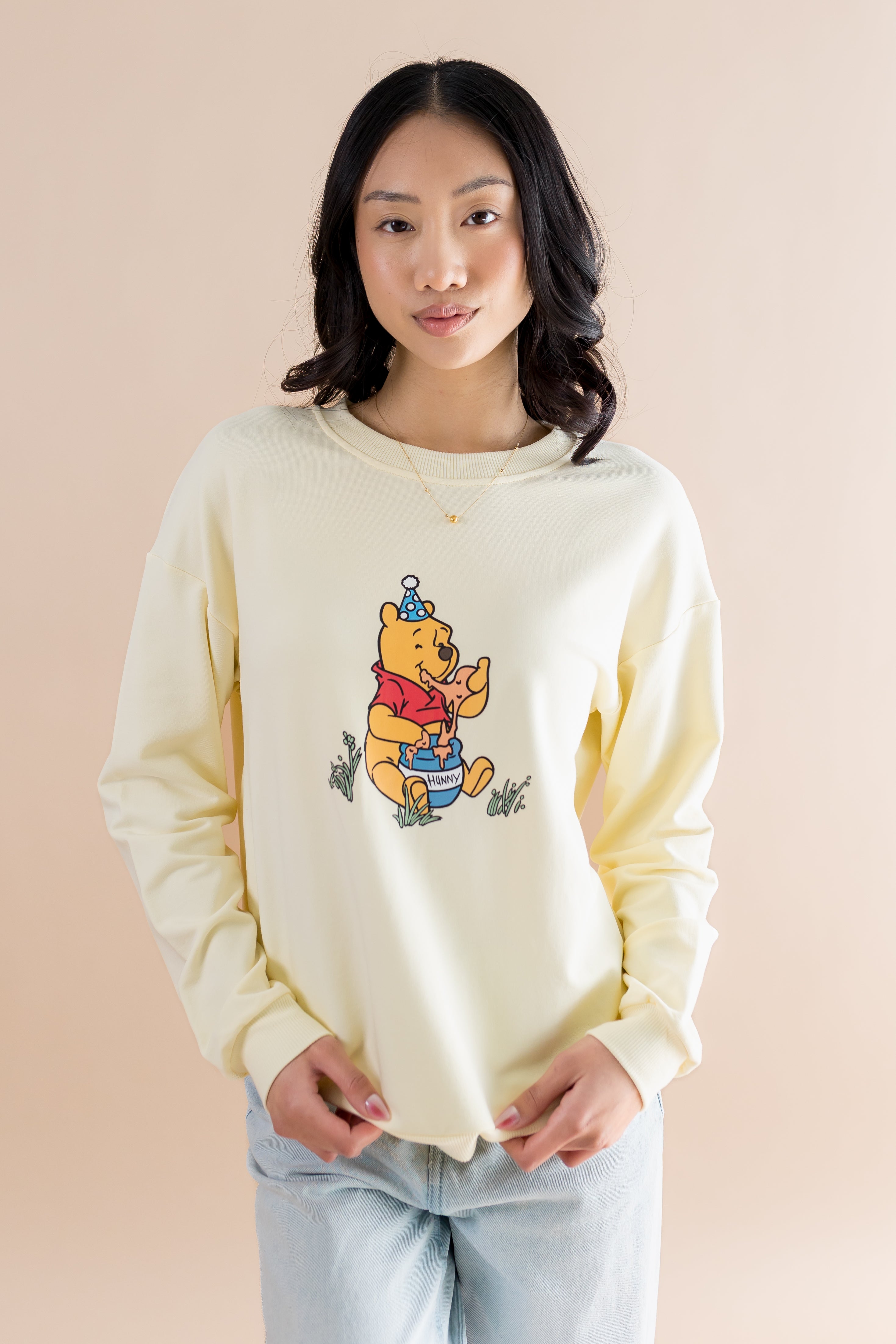 Person wearing a light-colored crewneck sweatshirt with a winnie the pooh graphic on a beige background 