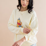 Woman wearing a light yellow sweatshirt with a cartoon character on a beige background