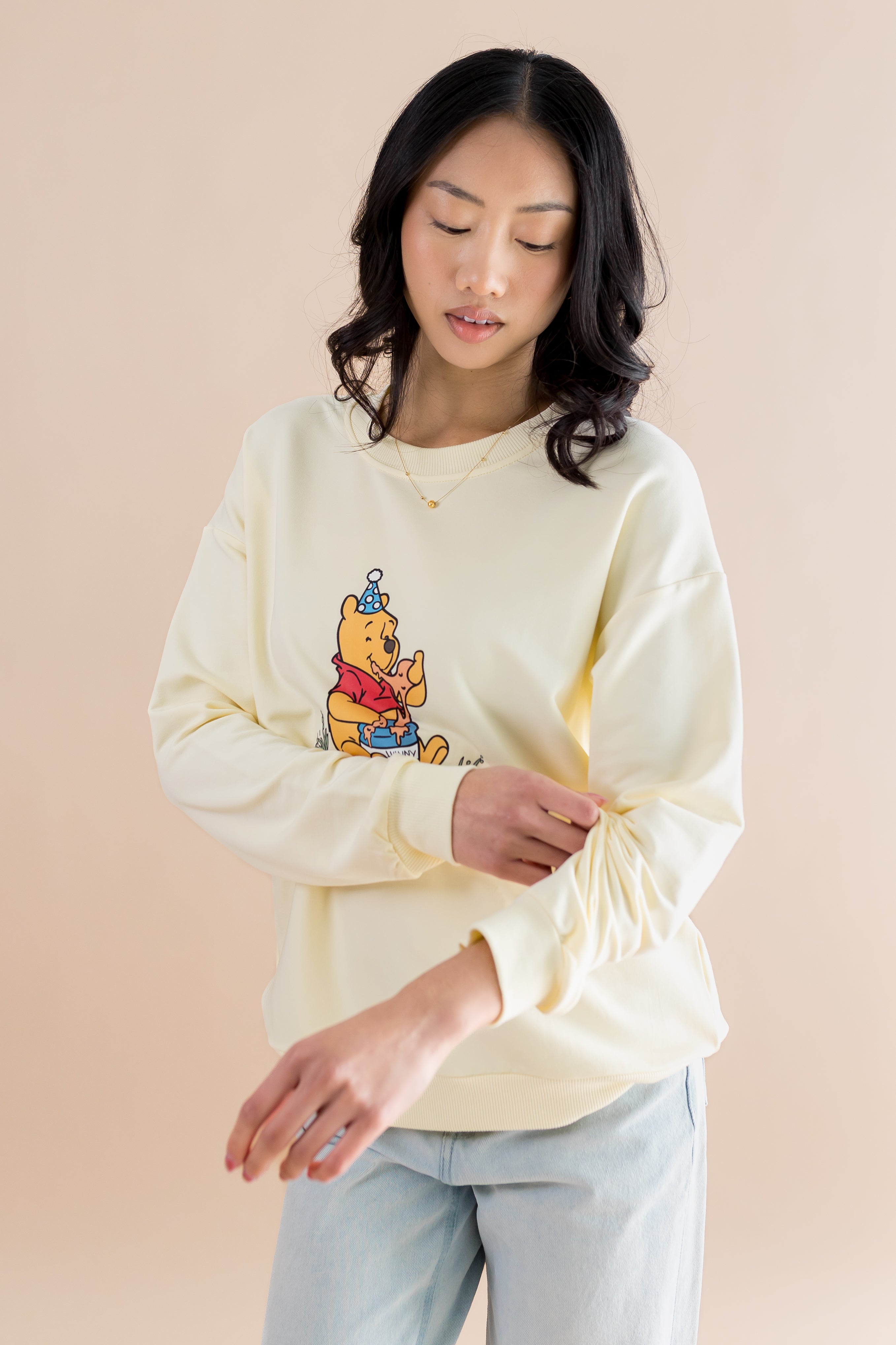Woman wearing a light yellow sweatshirt with a cartoon character on a beige background